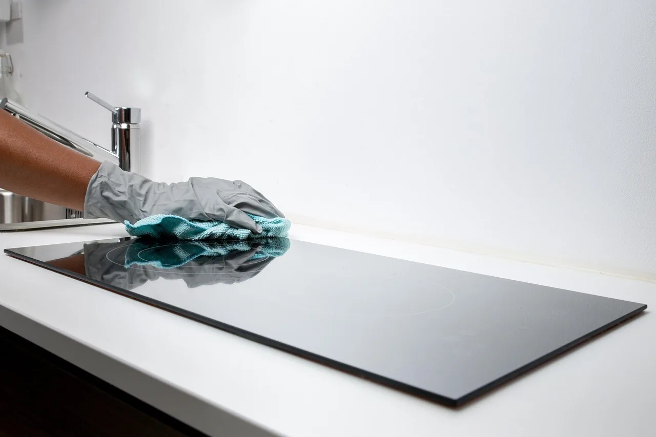 A gloved hand wiping a cooktop