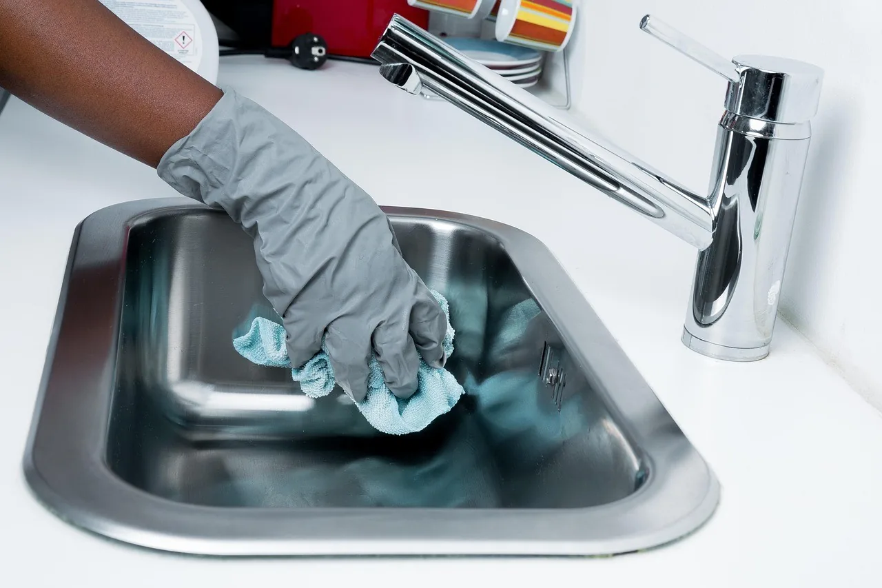 A gloved hand cleaning a kitchen sink