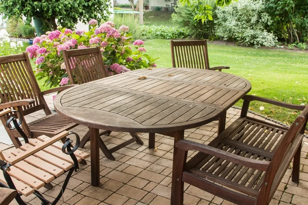 A timber outdoor table on clean pavers beside a garden